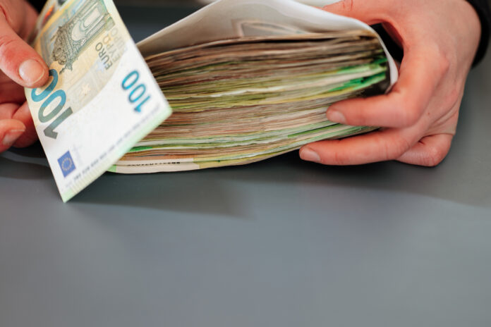 Ein Mann hält einen Geldumschlag mit vielen Geldscheinen darin. Ein 20.000 Euro Zuschuss soll kommen.