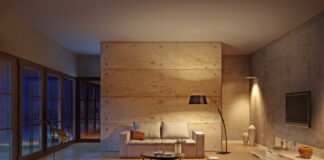 Ein sehr modern eingerichtetes Wohnzimmer in Beige mit Fernseher, Sofa, Lampe, Tisch und anderen Möbeln.