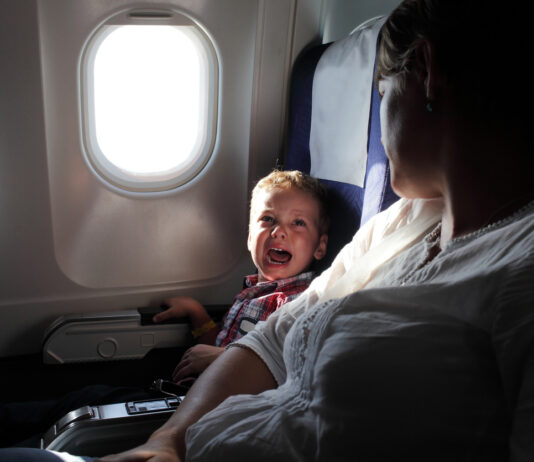 Ein kleiner Junge sitzt neben dem Platz seiner Mutter in einem Flugzeug und weint.