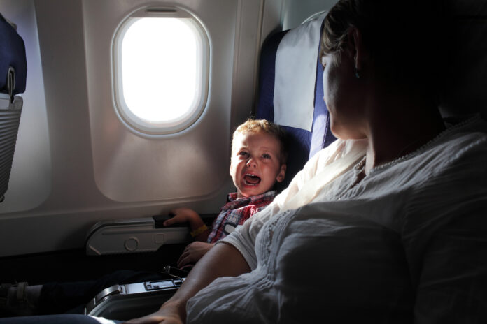 Ein kleiner Junge sitzt neben dem Platz seiner Mutter in einem Flugzeug und weint.
