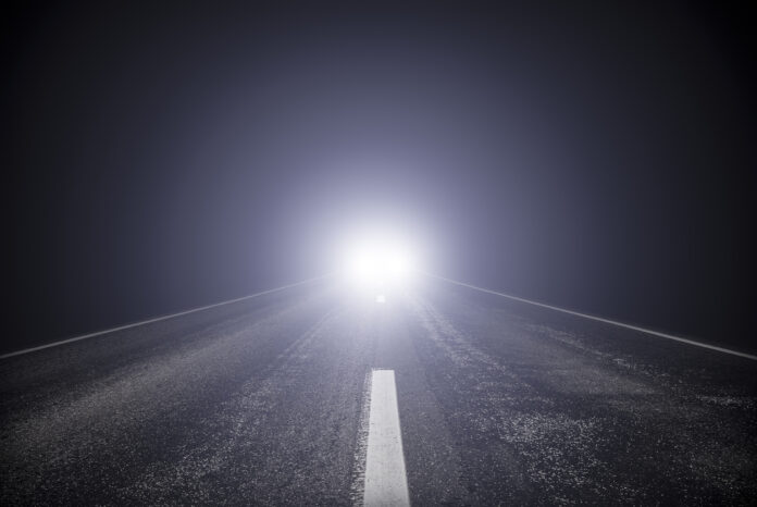 Ein Autofahrer hat das Fernlicht an und fährt auf einer Straße.