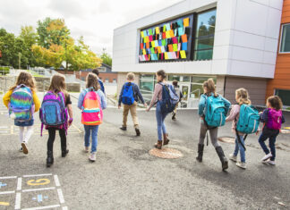 Mehrere Schüler sind mit ihren bunten Rucksäcken auf dem Weg zu ihrer Schule, wobei sie über den Pausenhof laufen und sich unterhalten