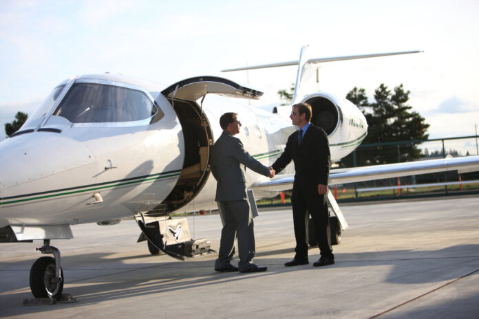 Zwei Männer schütteln sich an einem Privatflugzeug die Hand.