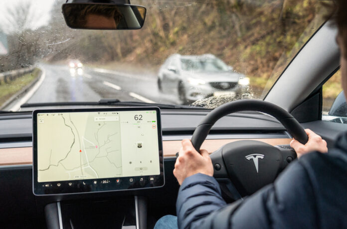 Un'auto Tesla che guida sulla strada sotto la pioggia.