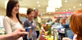 Drei Personen stehen an einer Kasse im Supermarkt. Einer bezahlt mit seiner EC-Karte.