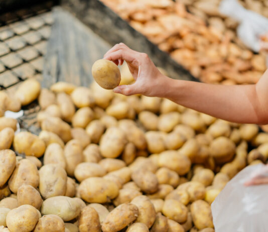 Eine Frau sucht sich eine von vielen rohen Kartoffeln im Supermarkt aus, um sie zu kaufen.
