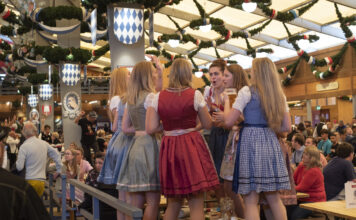 Eine Gruppe von Mädchen feiert im Dirndl auf dem Oktoberfest und tanzt auf den Tischen