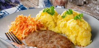 Eine Mahlzeit bestehend aus Kartoffelbrei, Karotten und Hackschnitzel liegt auf einem Teller mit Messer und Gabel