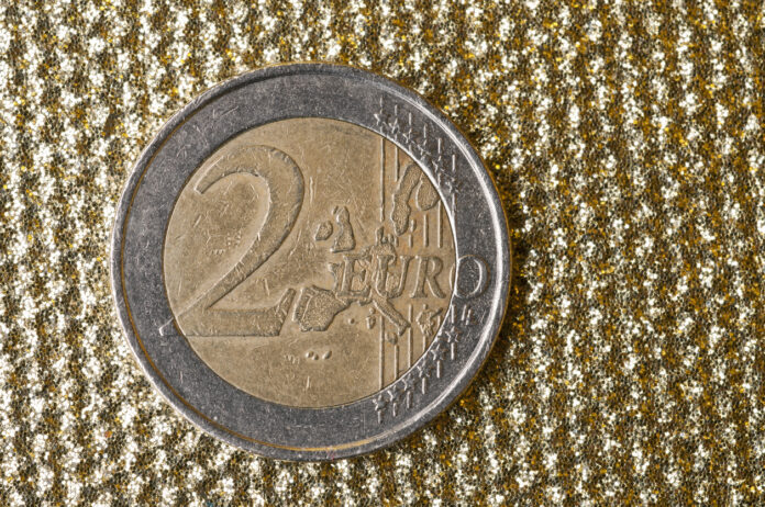 Eine 2-Euro-Münze liegt auf einer goldenen gewebten Tischdecke.