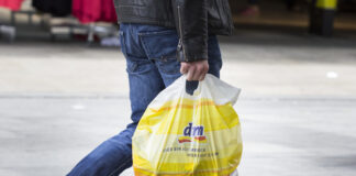 Eine Person trägt eine Plastiktüte von dm nach einem Einkauf über die Straße