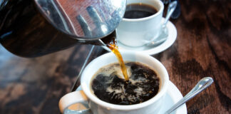 Kaffee wird aus einer Kanne in eine weiße Tasse gegossen. Kein Leitungswasser fürs Kaffeekochen verwenden.