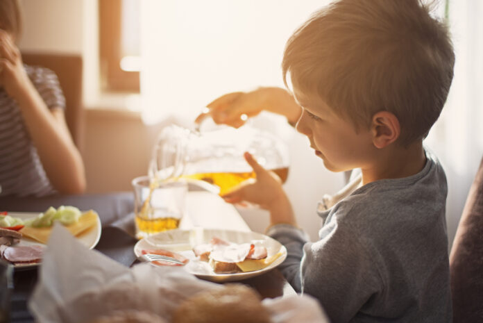 Ein Kind gießt ein Glas Apfelsaft ein.