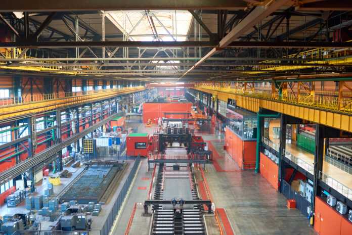 Eine Werkshalle von einem Unternehmen ist zu sehen. Die Maschinen stehen still und keine Arbeiter sind zu sehen. Das Unternehmen ist in der Industrie ansässig und stellt auf Fließbändern wichtige Produkte her.