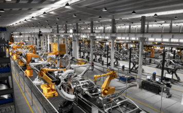 Eine Produktionsstraße eines Traditionsunternehmens in einer großen Halle, in der in einer Reihe viele elektrische Arme Autoteile an die richtige Stelle setzen.