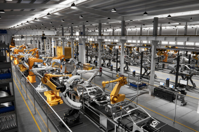Eine Produktionsstraße eines deutschen Autozulieferers, vielleicht auch eines Autobauers, ist zu sehen. In einer großen Halle stehen Roboter entlang der Produktionsstraße in der Montage.