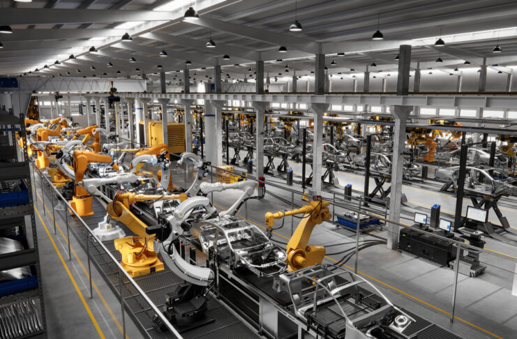 Eine Produktionsstraße eines Traditionsunternehmens in einer großen Halle, in der in einer Reihe viele elektrische Arme Autoteile an die richtige Stelle setzen.