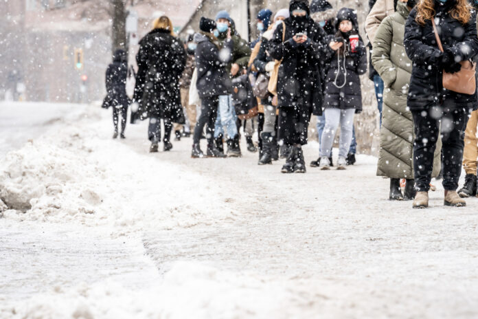 Viele Menschen stehen in einer Reihe im Winter bei Schnee in der Kälte an um etwas zu kaufen oder zu bekommen