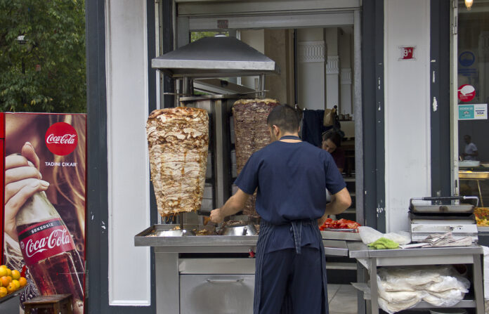 Ein Mitarbeiter steht an einem Dönerspieß und schneidet Fleisch für einen Döner ab