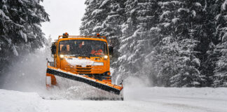 orangefarbener Schneeschieber schiebt Schnee auf zugeschneiter Straße