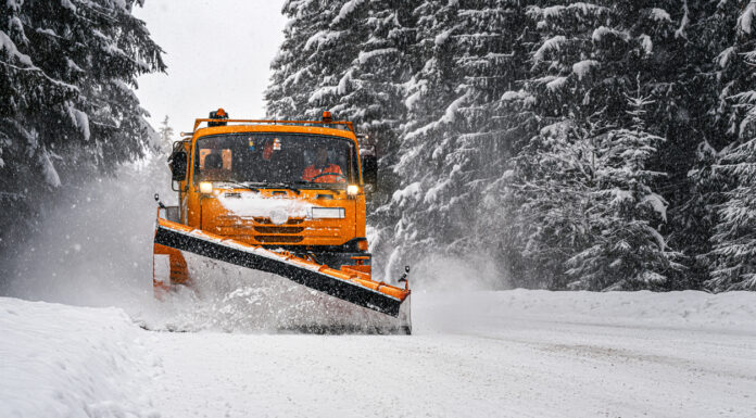 orangefarbener Schneeschieber schiebt Schnee auf zugeschneiter Straße