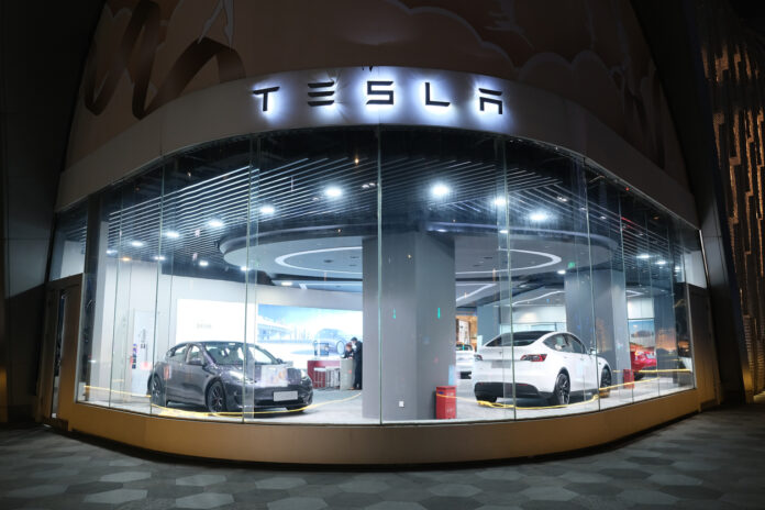 Verschiedene E-Autos als Tesla-Modell in einem beleuchteten Testla-Store hinter der Scheibe eines Autohändler