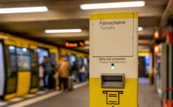 Im Vordergrund steht ein Automat, an dem man sein Ticket zur Kontrolle reinstecken muss. Im Hintergrund steigen Menschen in eine U-Bahn ein.