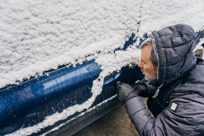 Ein Mann pustet gegen das Schloss seiner Autotür, die aufgrund von Frost zugefroren ist