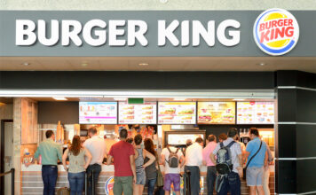 Eine lange Schlange von Menschen steht vor den einzelnen Bestelltresen von Burger King und warten darauf, dass sie dran sind, um ihre Bestellung aufzugeben.