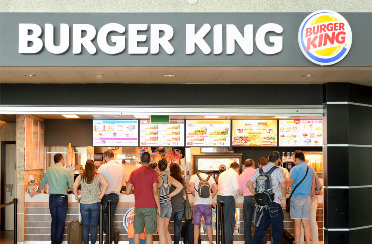 Eine lange Schlange von Menschen steht vor den einzelnen Bestelltresen von Burger King und warten darauf, dass sie dran sind, um ihre Bestellung aufzugeben.