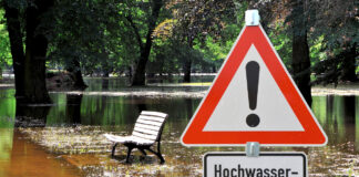 Hochwasserschäden und Überflutungen in einer Parkanlage mit einem Band Schild im Vordergrund