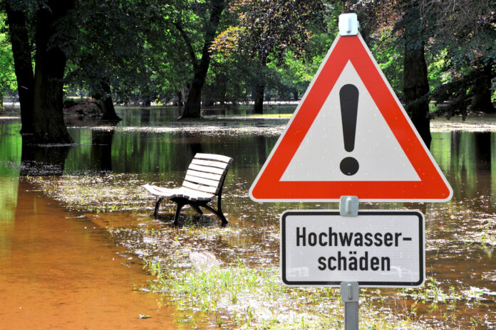 Hochwasserschäden und Überflutungen in einer Parkanlage mit einem Band Schild im Vordergrund