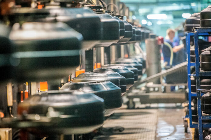 Viele Reifen in einem Produktionslager von einem Reifenhersteller. Hunderte Arbeiter stapeln die Autoreifen und geben sie weiter in die Verarbeitung. Es handelt sich um Reifen für Autos und Neufahrzeuge, die in den Verkauf gehen.