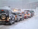 Viele Autos stehen im Stau auf einer zugeschneiten Straße.