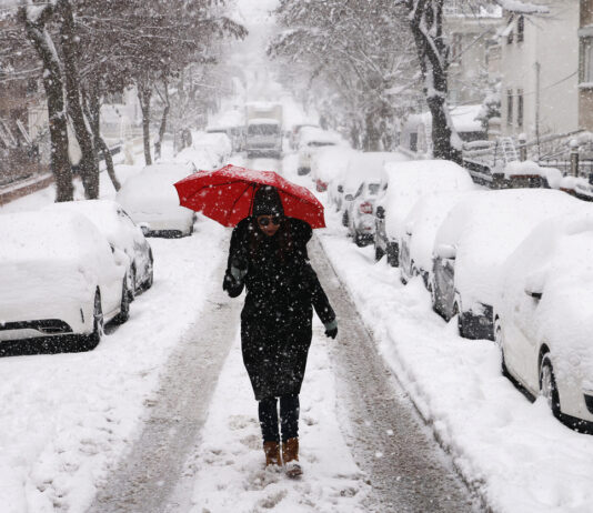 Frau mit Regenschirm spaziert im Schnee.