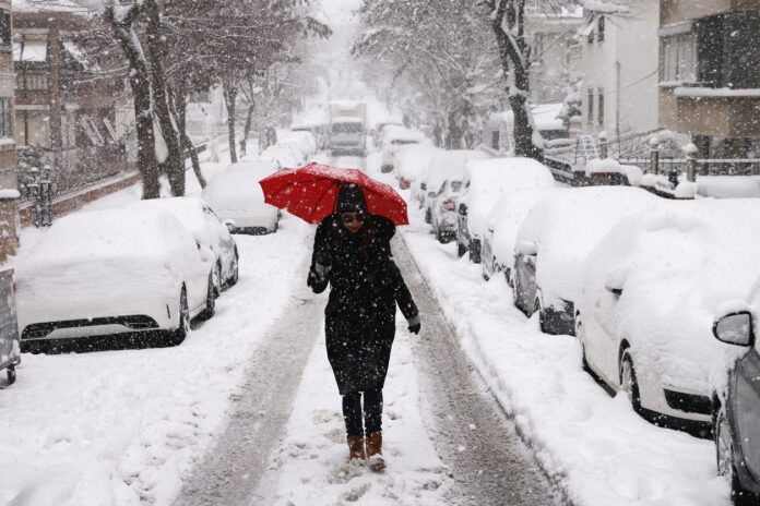 Frau mit Regenschirm spaziert im Schnee.