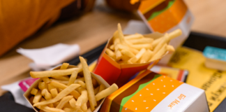 Auf einem Tisch in einem Restaurant steht ein McDonald's Menü. Auf dem Tablett liegen zwei Portionen Pommes, ein Big Mac und Servietten.