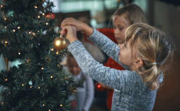 Ein Kind hängt eine Weihnachtskugel an den Weihnachtsbaum und dekoriert die Wohnung festlich