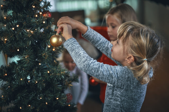Ein Kind hängt eine Weihnachtskugel an den Weihnachtsbaum und dekoriert die Wohnung festlich