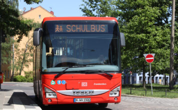 Ein großer roter Schulbus an einer Haltestelle. Der Bus ist an der Aufschrift Schulbus zu erkennen. Er wartet darauf, dass Schülerinnen und Schüler einsteigen, um nach Hause oder zur Schule gefahren zu werden. Dieser Bus gehört zum öffentlichen Personennahverkehr.
