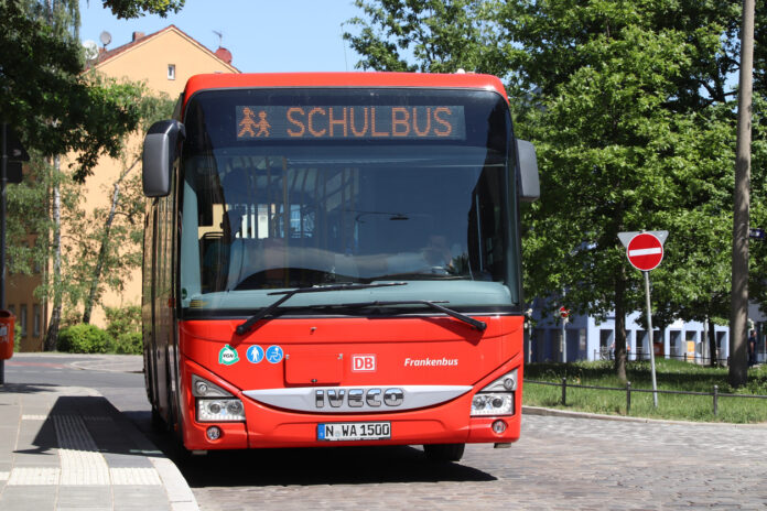 Ein großer roter Schulbus an einer Haltestelle. Der Bus ist an der Aufschrift "Schulbus" zu erkennen. Er wartet darauf, dass Schüler einsteigen, um nach Hause oder zur Schule gefahren zu werden. Dieser Bus gehört zum öffentlichen Personennahverkehr.