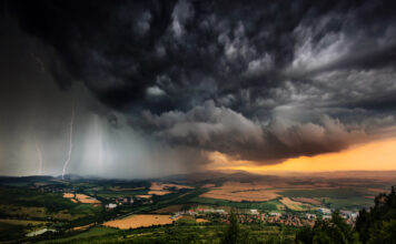 Ein schweres Gewitter fegt über eine Landschaft. Das Gewitter bringt Blitz, Donner, Sturm und Hagel mit sich. Am Himmel ziehen dunkle, bedrohliche Wolken auf.