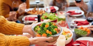 Eine Frau reicht an einem Tisch einem Familienmitglied eine Schüssel mit Gemüse.