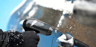 Eine eingefrorene Autotür wird von einer Hand mit einem Föhn aufgetaut.