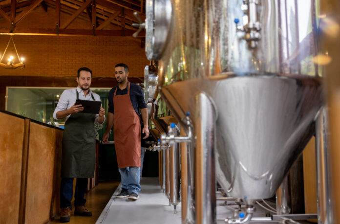 Zwei Männer stehen in einer Brauerei, in der ein Getränk hergestellt wird.