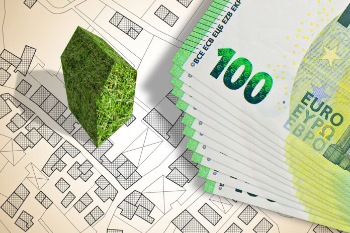 Ein Stapel mit Hundert-Euroscheinen und daneben ein grünes Haus