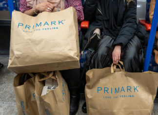 Frauen sitzen in der Straßenbahn und halten ihre Einkäufe vor sich. Diese befinden sich in Primark-Tüten aus Papier. Die Frauen sind elegant gekleidet.