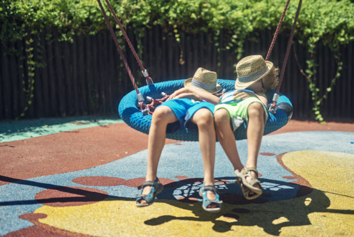 Zwei Kinder entspannen auf der Schaukel in der Sonne.