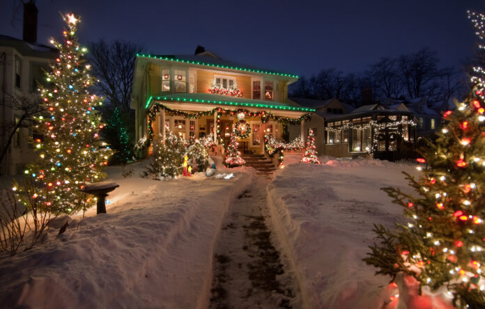 Ein geschmücktes Haus mit Weihnachtsdeko. Daneben steht ein Weihnachtsbaum und davor liegt Schnee.