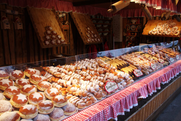 Eine Auslage in einer Traditionsbäckerei, in der auch typisches Gebäck aus Deutschland, zum Beispiel der Berliner, zu finden ist. Der vordere Bereich der Auslage ist mit einem rot-weißen Stoff dekoriert.