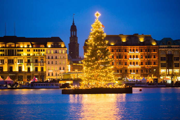 Ein Weihnachtsbaum steht im Hafen auf einer Plattform und ist hell beleuchtet.